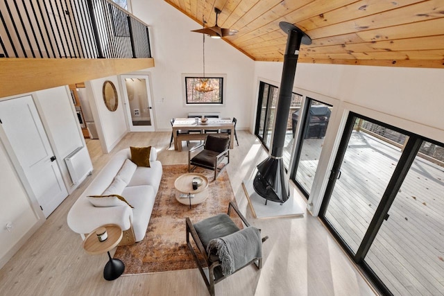 living room featuring a wood stove, high vaulted ceiling, light hardwood / wood-style floors, a chandelier, and wooden ceiling