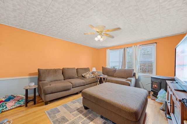 living room with ceiling fan, a wood stove, and light hardwood / wood-style floors