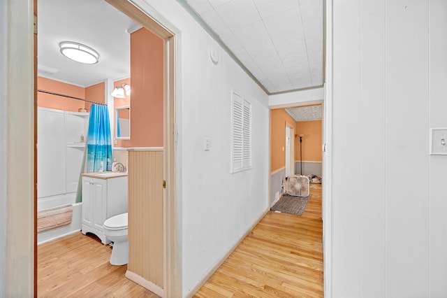 corridor with wood walls, sink, and light hardwood / wood-style flooring