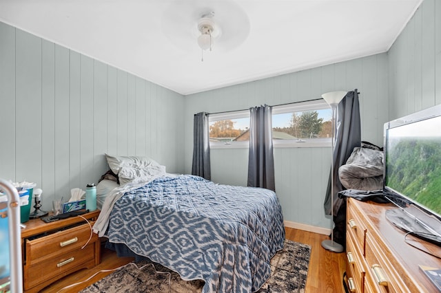 bedroom featuring hardwood / wood-style floors, ceiling fan, and wood walls