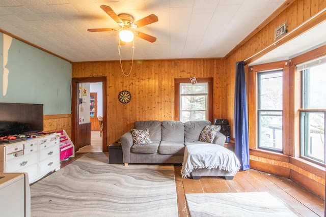 living room with a wealth of natural light, ceiling fan, wooden walls, and light wood-type flooring