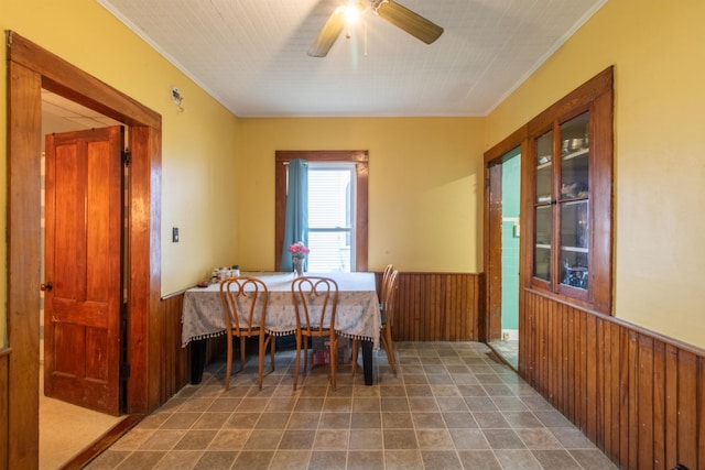 dining room featuring crown molding, wooden walls, and ceiling fan