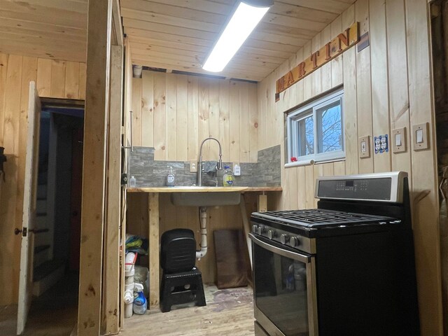 kitchen featuring light hardwood / wood-style floors, wooden walls, sink, wooden ceiling, and stainless steel gas range oven
