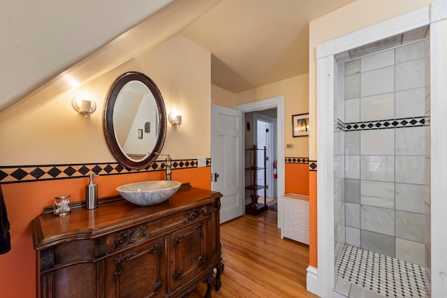 bathroom featuring wood-type flooring, vanity, a tile shower, and lofted ceiling