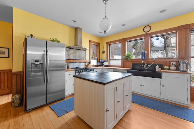 kitchen with stainless steel appliances, a center island, wall chimney exhaust hood, hanging light fixtures, and white cabinetry