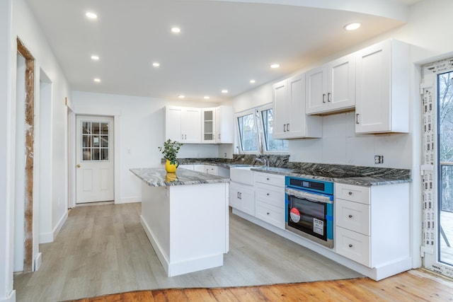 kitchen with white cabinets, light hardwood / wood-style floors, and stainless steel oven