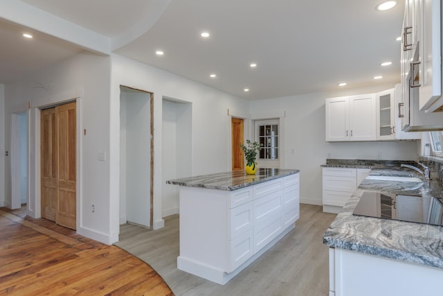 kitchen featuring black electric cooktop, dark stone counters, light hardwood / wood-style flooring, a kitchen island, and white cabinets