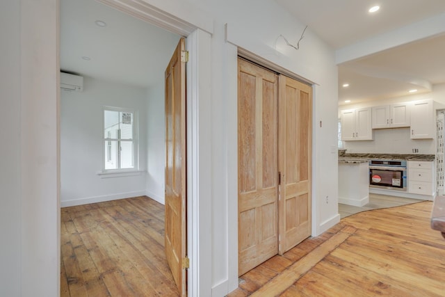 corridor with a wall mounted AC and light hardwood / wood-style flooring