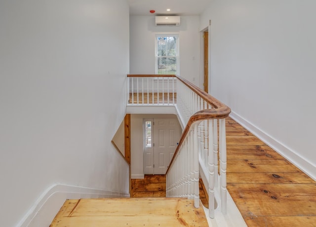 stairway with wood-type flooring and a wall mounted air conditioner