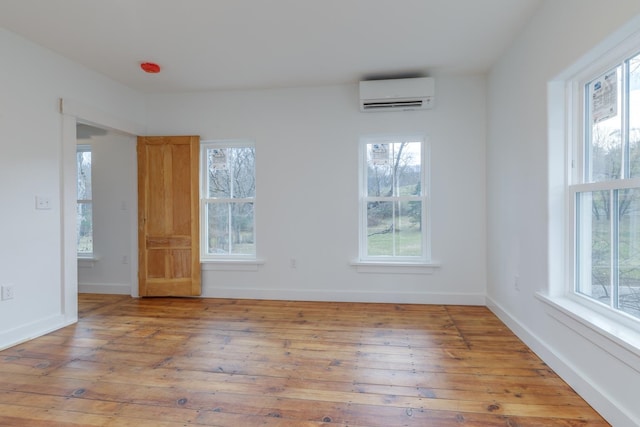 empty room with a wealth of natural light, a wall mounted AC, and light hardwood / wood-style floors