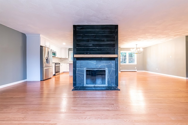 unfurnished living room with a tiled fireplace, a baseboard radiator, light hardwood / wood-style floors, and a notable chandelier