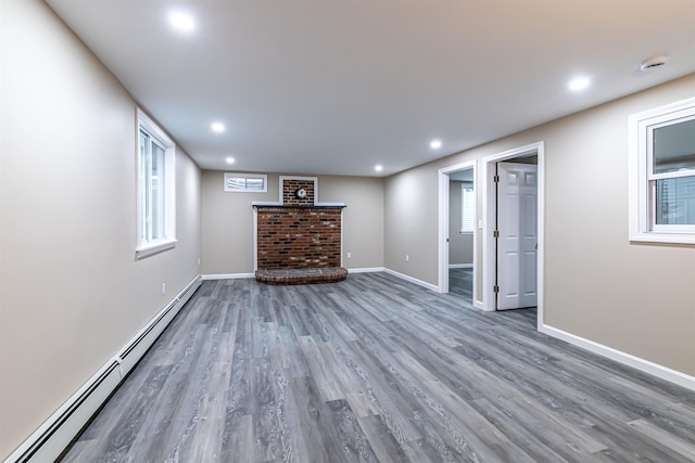 basement with dark hardwood / wood-style flooring, a brick fireplace, and a baseboard heating unit