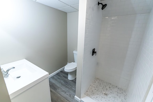 bathroom featuring tiled shower, wood-type flooring, toilet, a paneled ceiling, and vanity