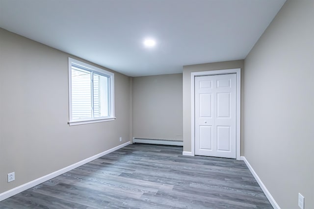 unfurnished bedroom featuring dark wood-type flooring, baseboard heating, and a closet