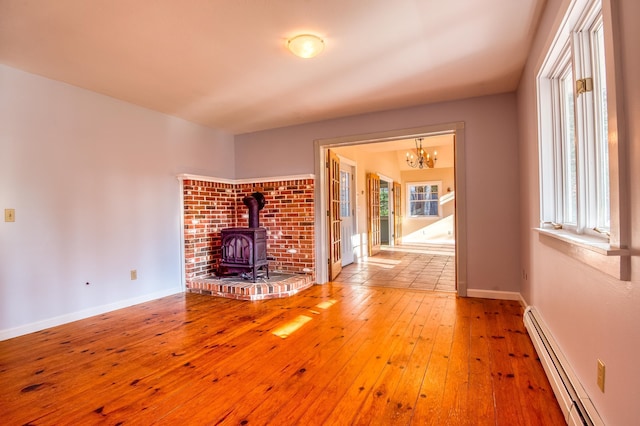 unfurnished living room featuring hardwood / wood-style flooring, baseboard heating, and a wood stove