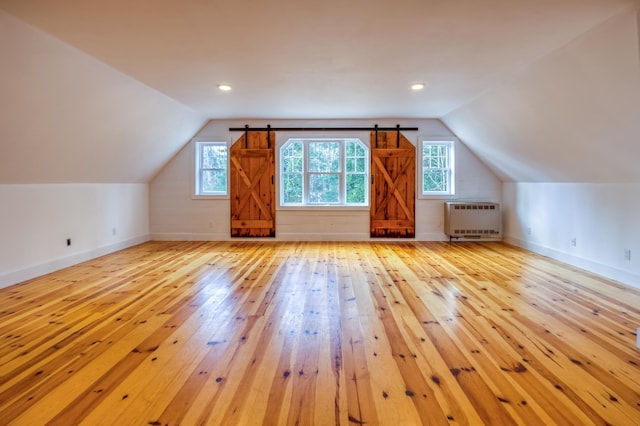 additional living space with radiator, lofted ceiling, and light hardwood / wood-style floors