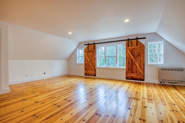 additional living space featuring vaulted ceiling, radiator heating unit, and light hardwood / wood-style floors