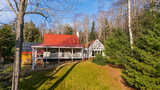 rear view of property featuring a lawn, solar panels, and covered porch