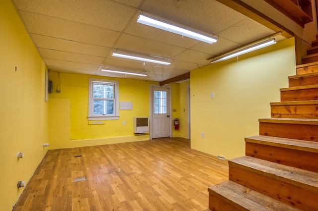 basement with light wood-type flooring, a paneled ceiling, and heating unit