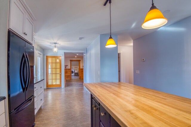 kitchen with wood counters, black fridge, hanging light fixtures, washing machine and dryer, and white cabinets