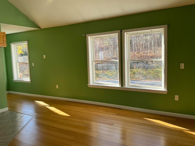 spare room featuring lofted ceiling, a healthy amount of sunlight, and light hardwood / wood-style flooring