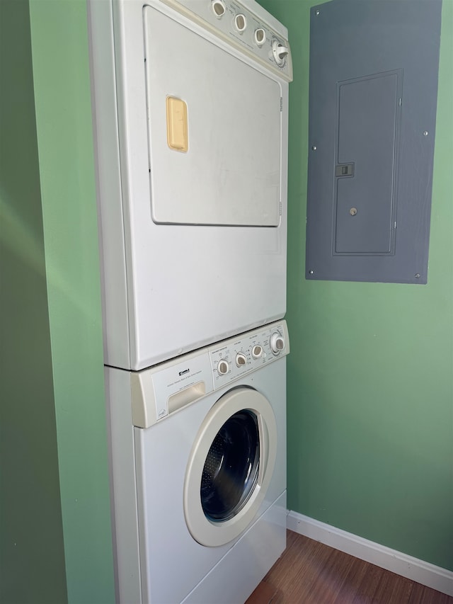 laundry room featuring stacked washer / drying machine, dark wood-type flooring, and electric panel