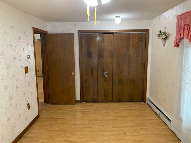 unfurnished bedroom with light wood-type flooring, a baseboard radiator, a textured ceiling, and a closet