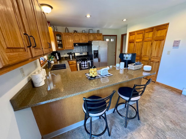 kitchen with appliances with stainless steel finishes, sink, a breakfast bar area, dark stone countertops, and kitchen peninsula