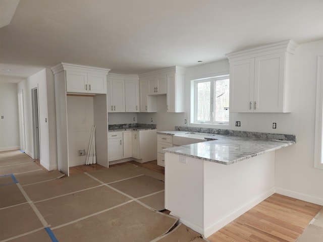 kitchen featuring kitchen peninsula, white cabinets, light stone counters, and light hardwood / wood-style flooring