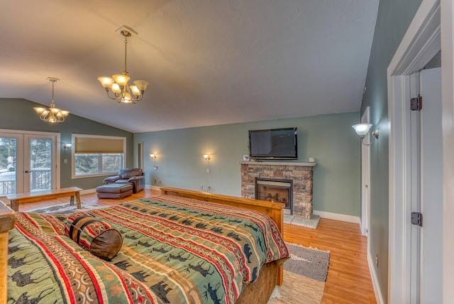 bedroom with vaulted ceiling, a stone fireplace, a notable chandelier, light wood-type flooring, and french doors