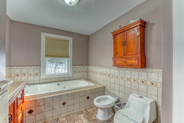 bathroom with tile walls, a bidet, vanity, toilet, and a relaxing tiled tub