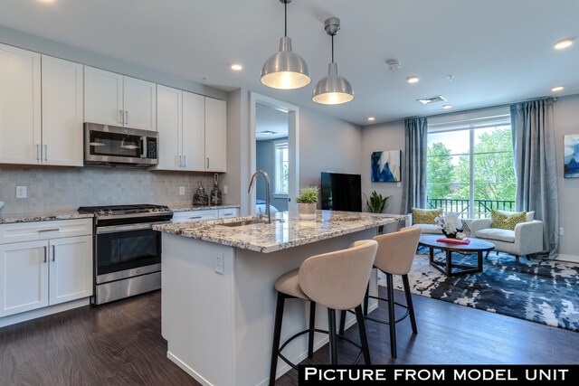 kitchen with appliances with stainless steel finishes, hanging light fixtures, a center island with sink, and white cabinets