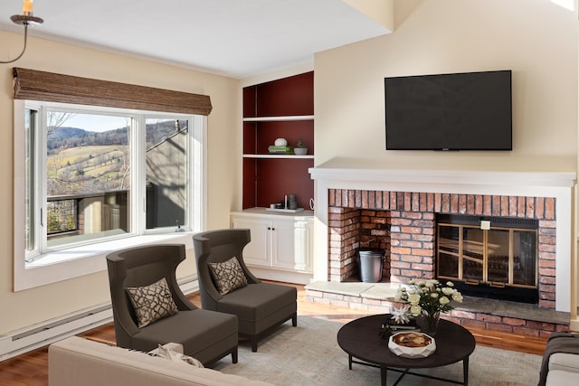 living room featuring built in features, light wood-type flooring, a brick fireplace, and a baseboard radiator