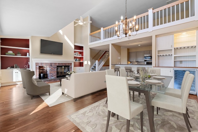 dining space with a brick fireplace, hardwood / wood-style floors, ceiling fan with notable chandelier, and high vaulted ceiling