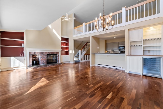 unfurnished living room featuring a baseboard heating unit, ceiling fan with notable chandelier, high vaulted ceiling, dark hardwood / wood-style floors, and a fireplace