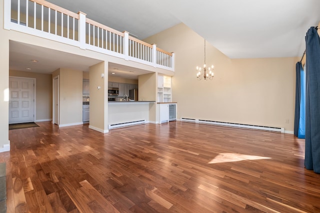 unfurnished living room with a baseboard heating unit, a towering ceiling, wood-type flooring, and a chandelier