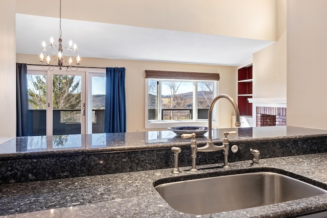 kitchen featuring sink, dark stone countertops, an inviting chandelier, hanging light fixtures, and built in features