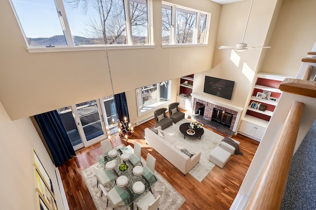 living room featuring a high ceiling, wood-type flooring, ceiling fan, and a fireplace