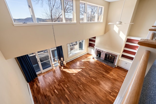 unfurnished living room with hardwood / wood-style flooring, a fireplace, ceiling fan, and a high ceiling