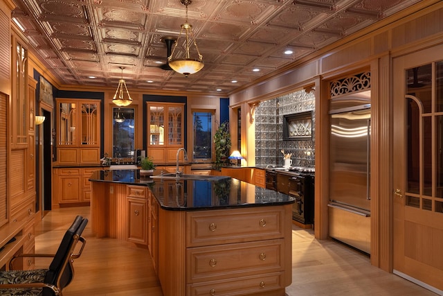 kitchen with light wood-type flooring, a center island with sink, decorative light fixtures, and dark stone countertops