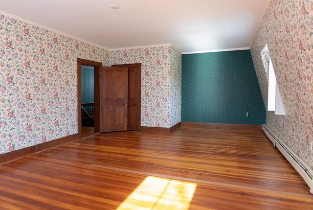 empty room featuring hardwood / wood-style floors, crown molding, and a baseboard heating unit