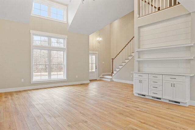 276 Sterling Dr, Laconia, NH 03246 - unfurnished living room with a towering ceiling, stairs, a chandelier, light wood-style flooring, and baseboards