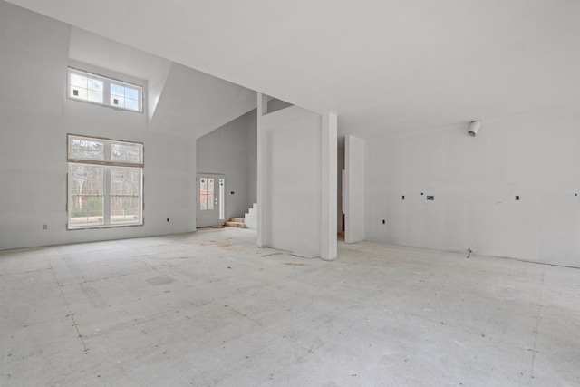 unfurnished living room with high vaulted ceiling and a healthy amount of sunlight