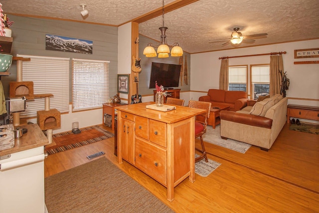 kitchen with ceiling fan with notable chandelier, light wood-type flooring, a textured ceiling, decorative light fixtures, and a kitchen bar