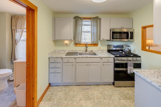 kitchen with light stone countertops, a wealth of natural light, a sink, and appliances with stainless steel finishes