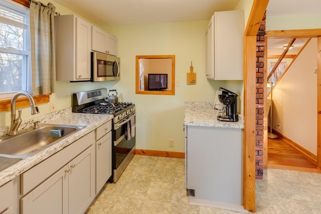 kitchen with white cabinets, baseboards, stainless steel appliances, and a sink