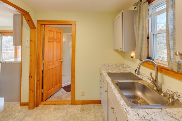 kitchen featuring white cabinets, baseboards, and a sink