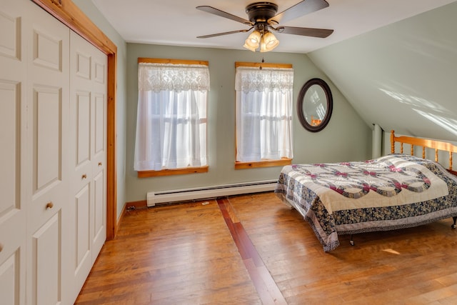 bedroom with vaulted ceiling, baseboard heating, a closet, ceiling fan, and wood-type flooring