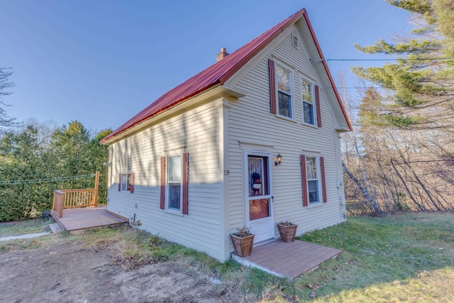 exterior space with a lawn, a chimney, metal roof, and a deck