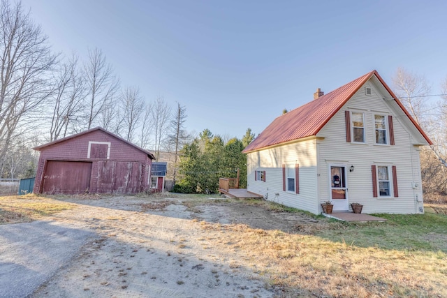view of front of property featuring a detached garage, a chimney, an outdoor structure, metal roof, and a barn